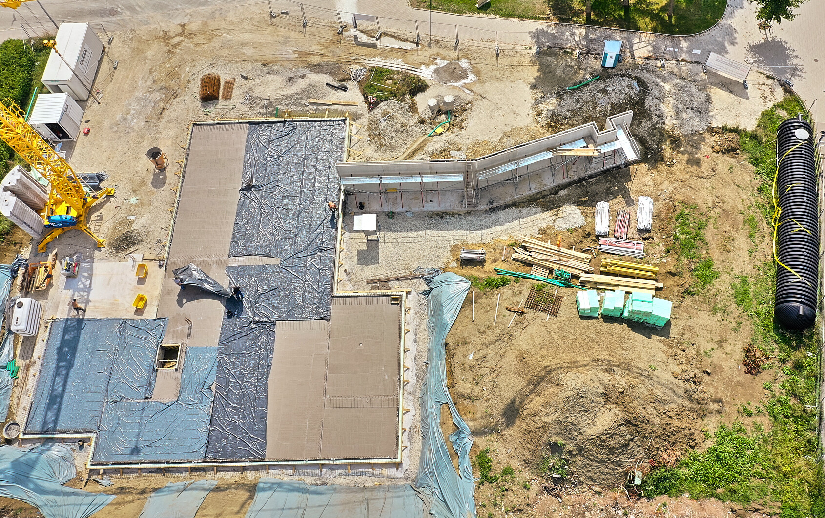 Bird’s eye view of a construction site: yellow crane, concrete foundation, and material stacks.