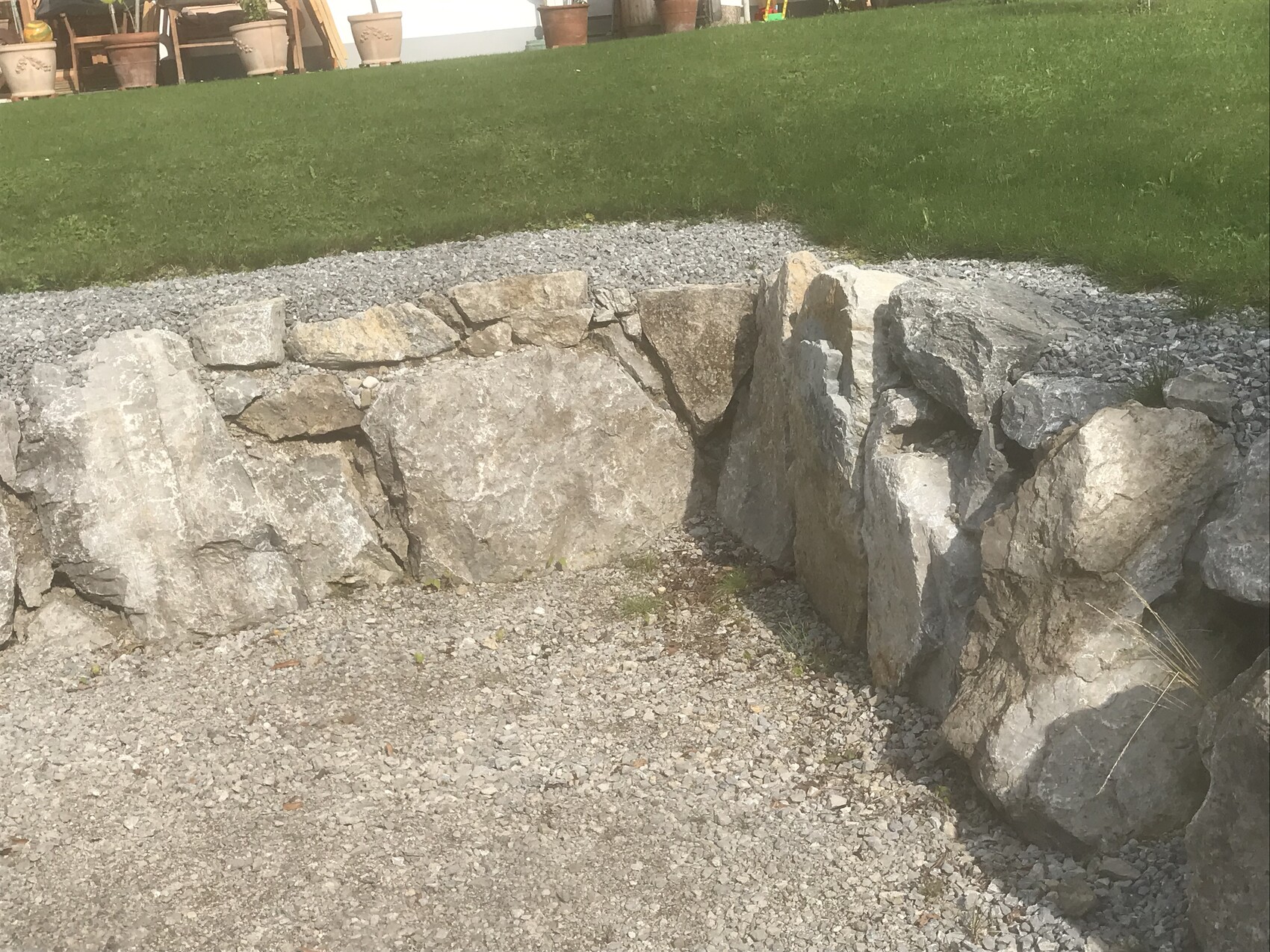 Natursteinmauer am Kiesweg im Garten mit grünem Rasen dahinter.