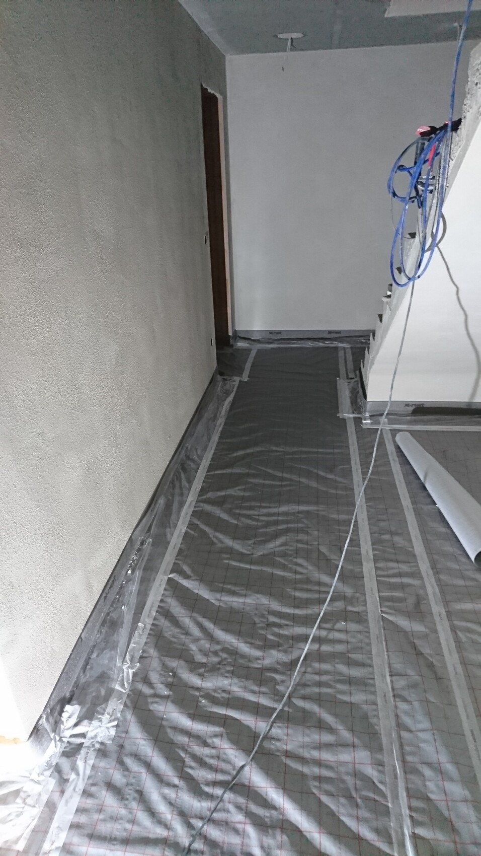 Construction site: floor with protective film, loose cables on the ceiling, bright corridor.