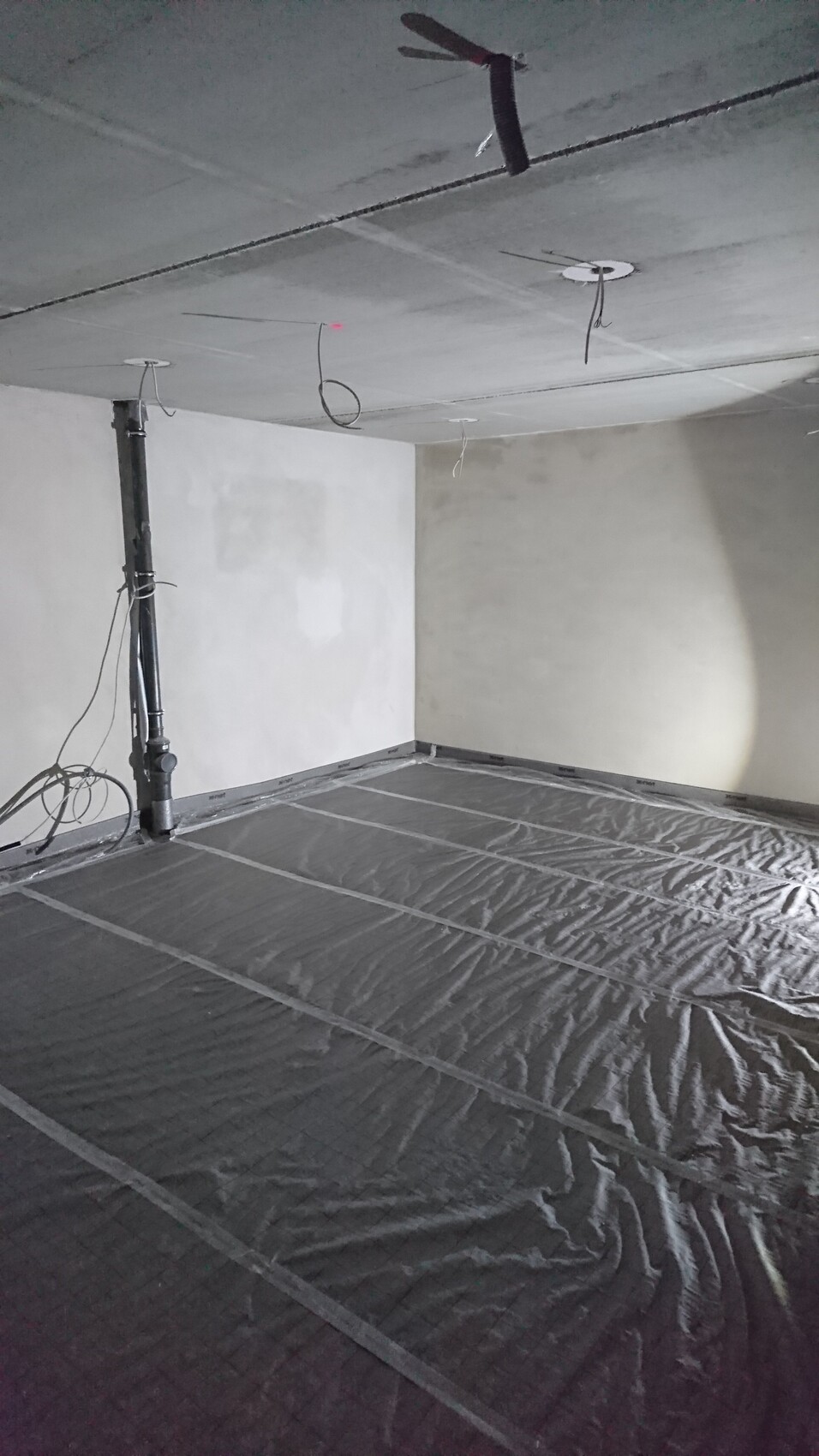 Unfinished renovation room: ceiling with cables and pipes; floor with black plastic sheeting.