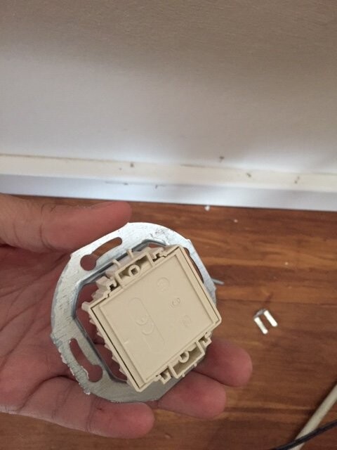 Person holding flush-mounted light switch housing in metal box over wooden floor