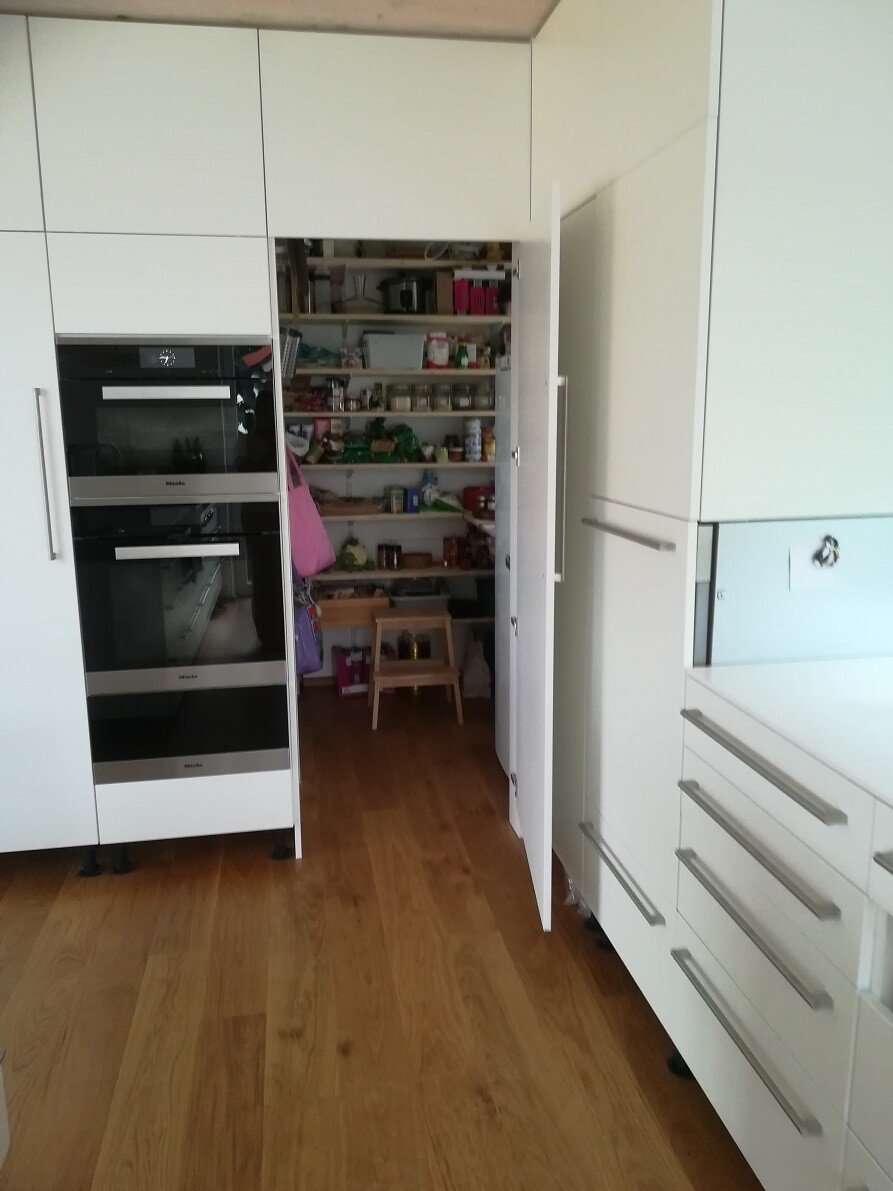 Modern white kitchen unit with built-in appliances and open pantry shelves