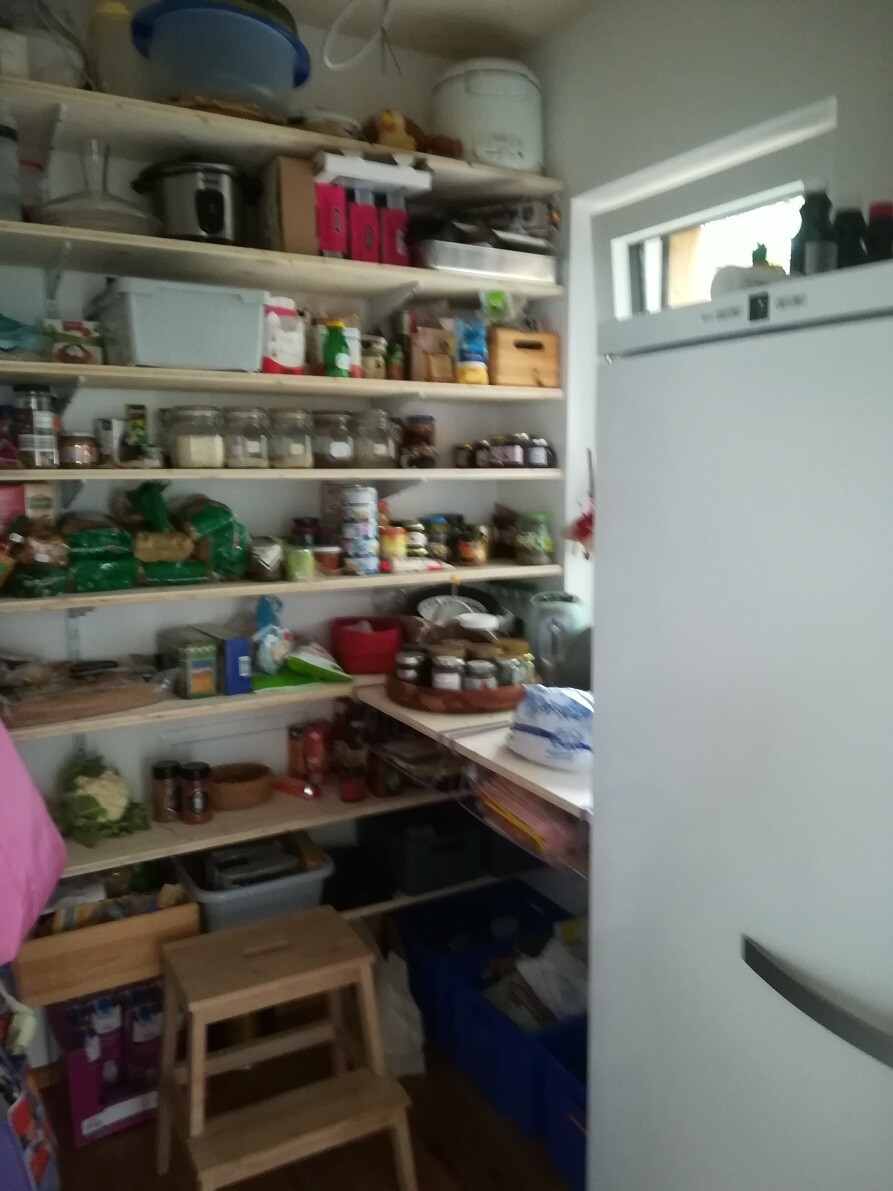 Pantry with open shelves full of jars, cans, and storage containers; fridge on the right.