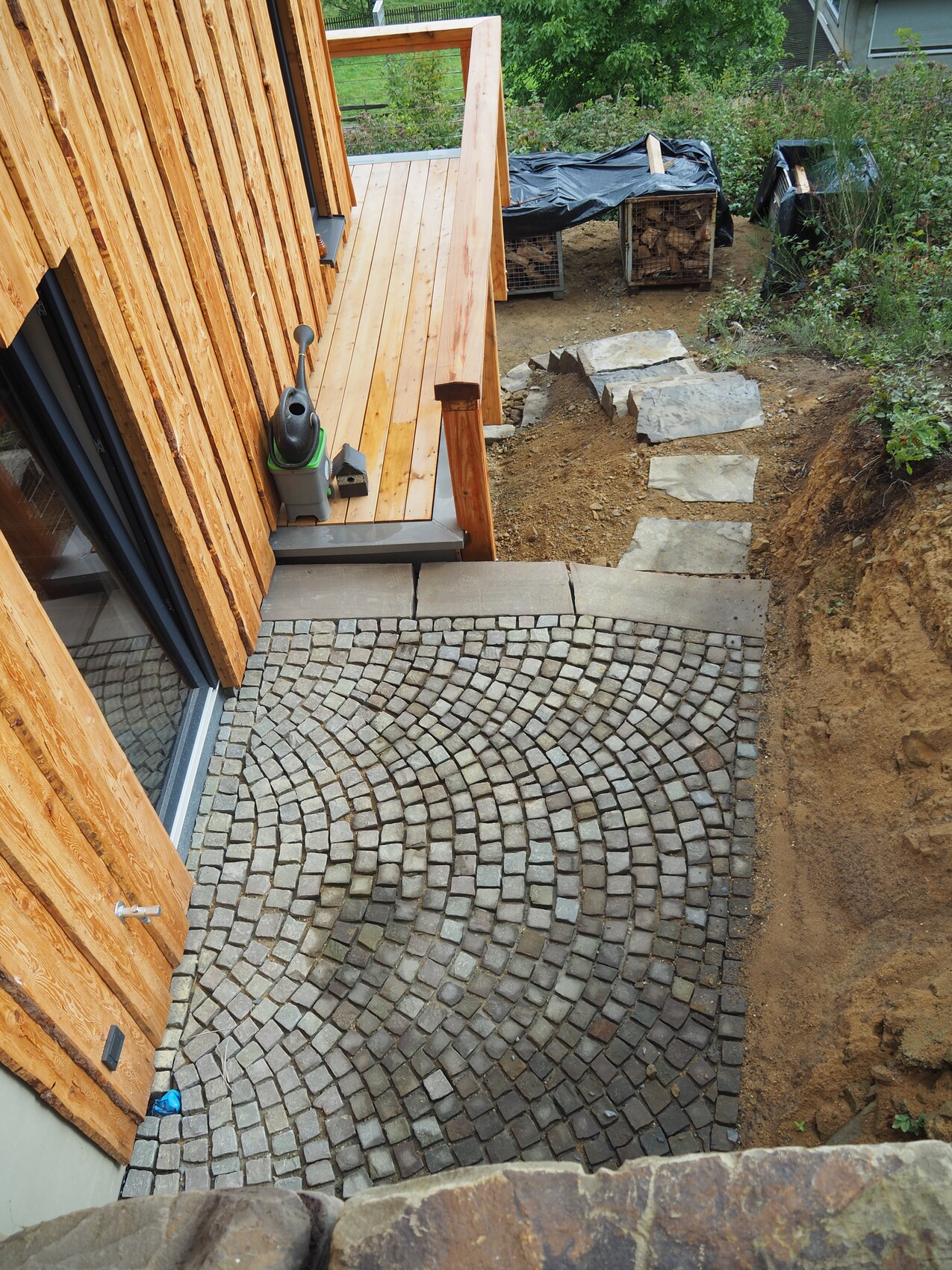 Wooden house construction site with curved stone paving of grey stones, wooden deck and path.