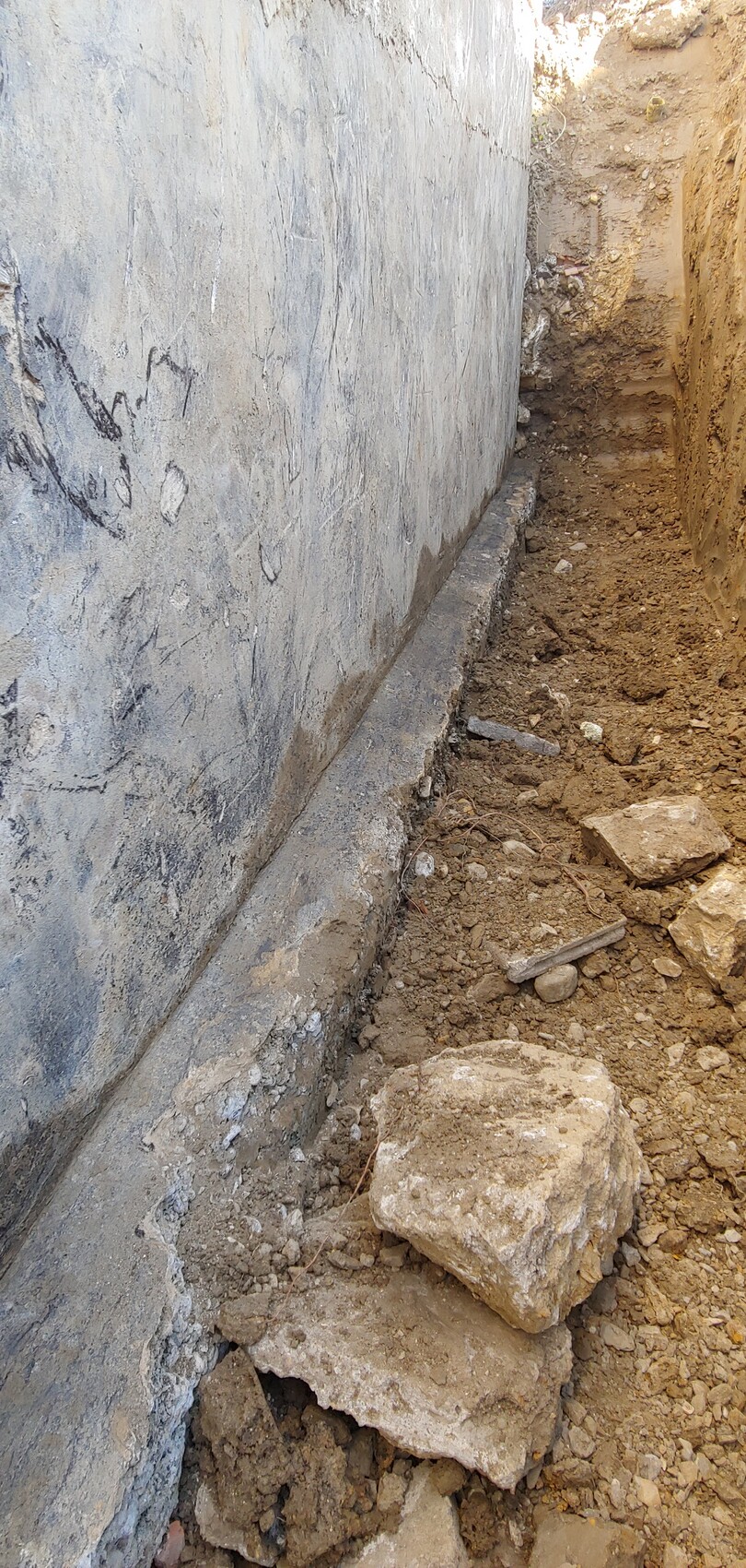 Deep excavation next to concrete wall with soil and stones, prepared for the foundation