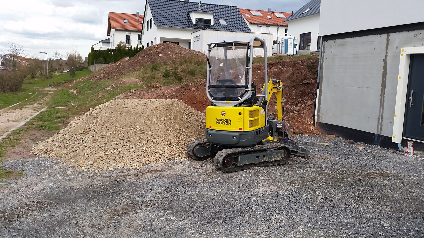 Small yellow construction machine (mini excavator) on a construction site next to a new build with excavation