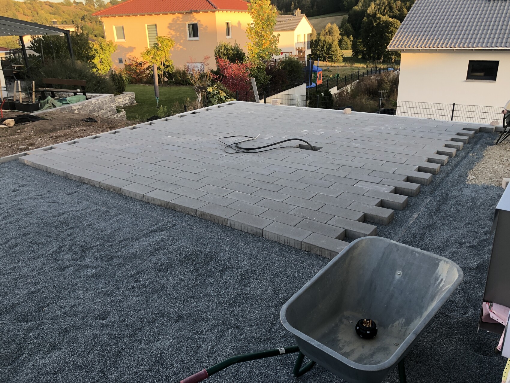 Roof terrace: gray paving stones are being laid; wheelbarrow in the foreground.