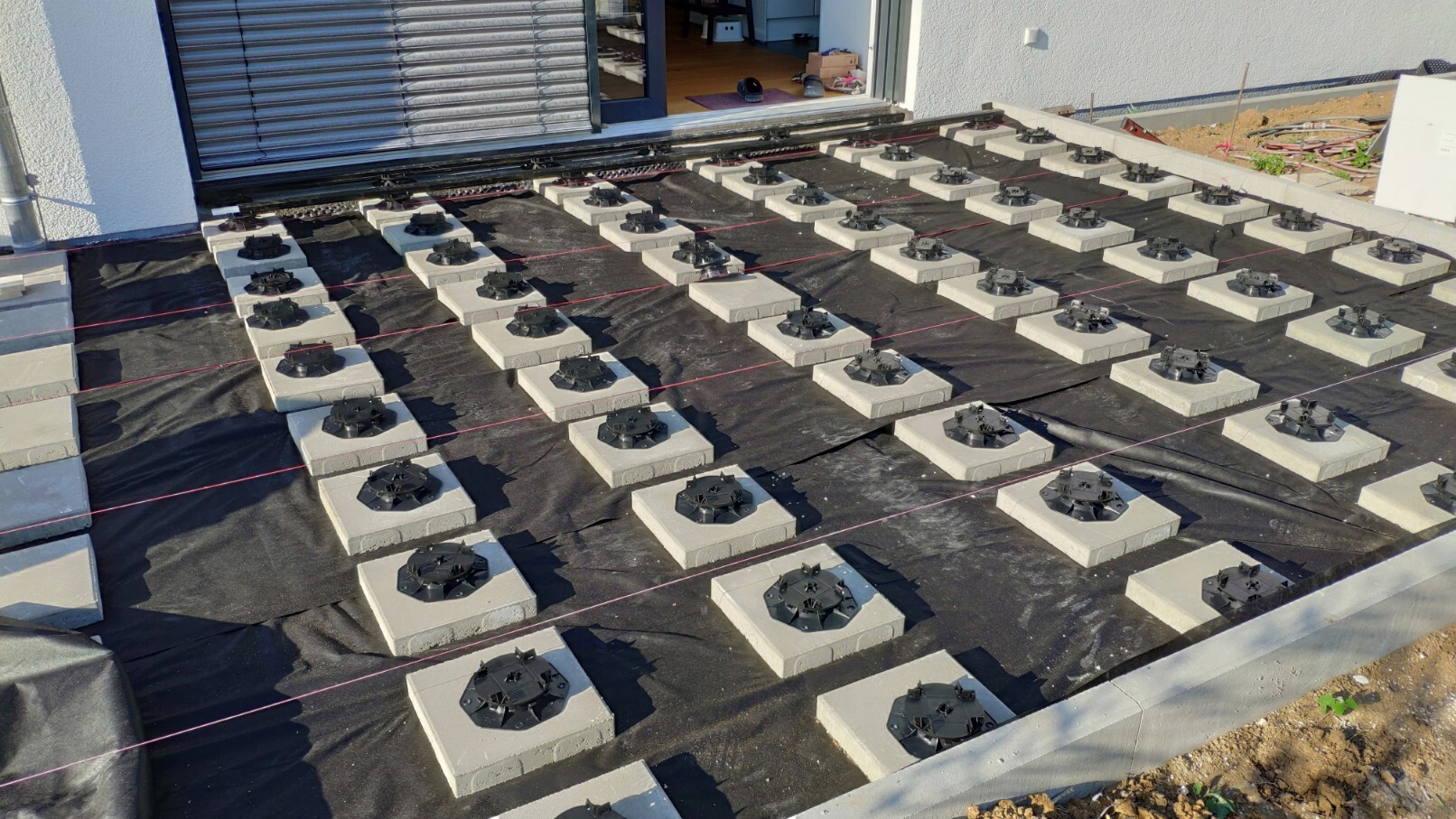 Outdoor area of a construction site with concrete foundations, mounting rings, and red strings.