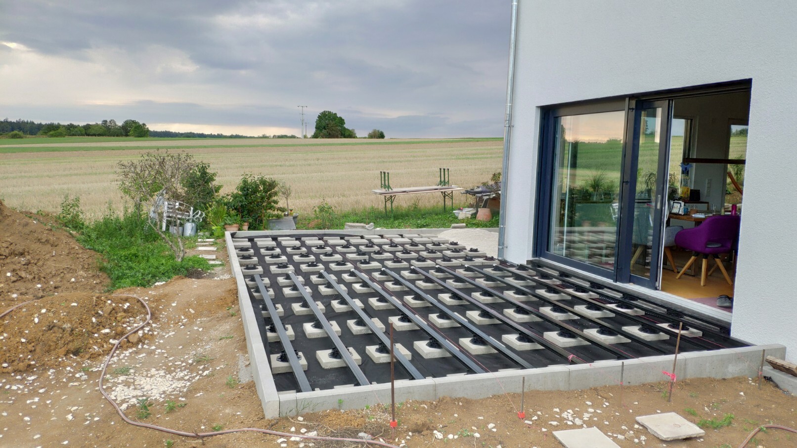 Exterior view of a house with glass facade; terrace substructure under construction in front of fields.
