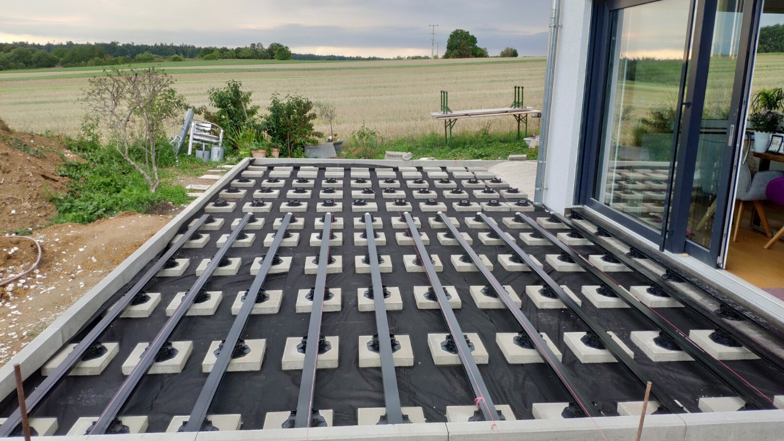Terrace under construction: heating pipes on styrofoam base, black supports, glass door to the right.