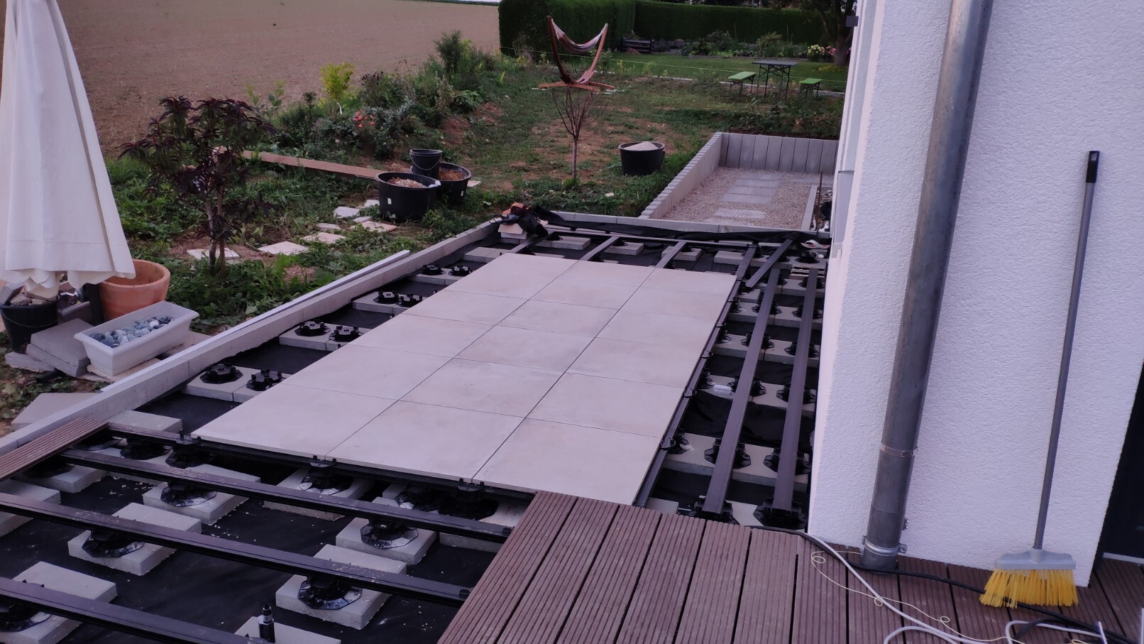 Outdoor area: terrace tiles being laid on substructure; garden with plants in the background.