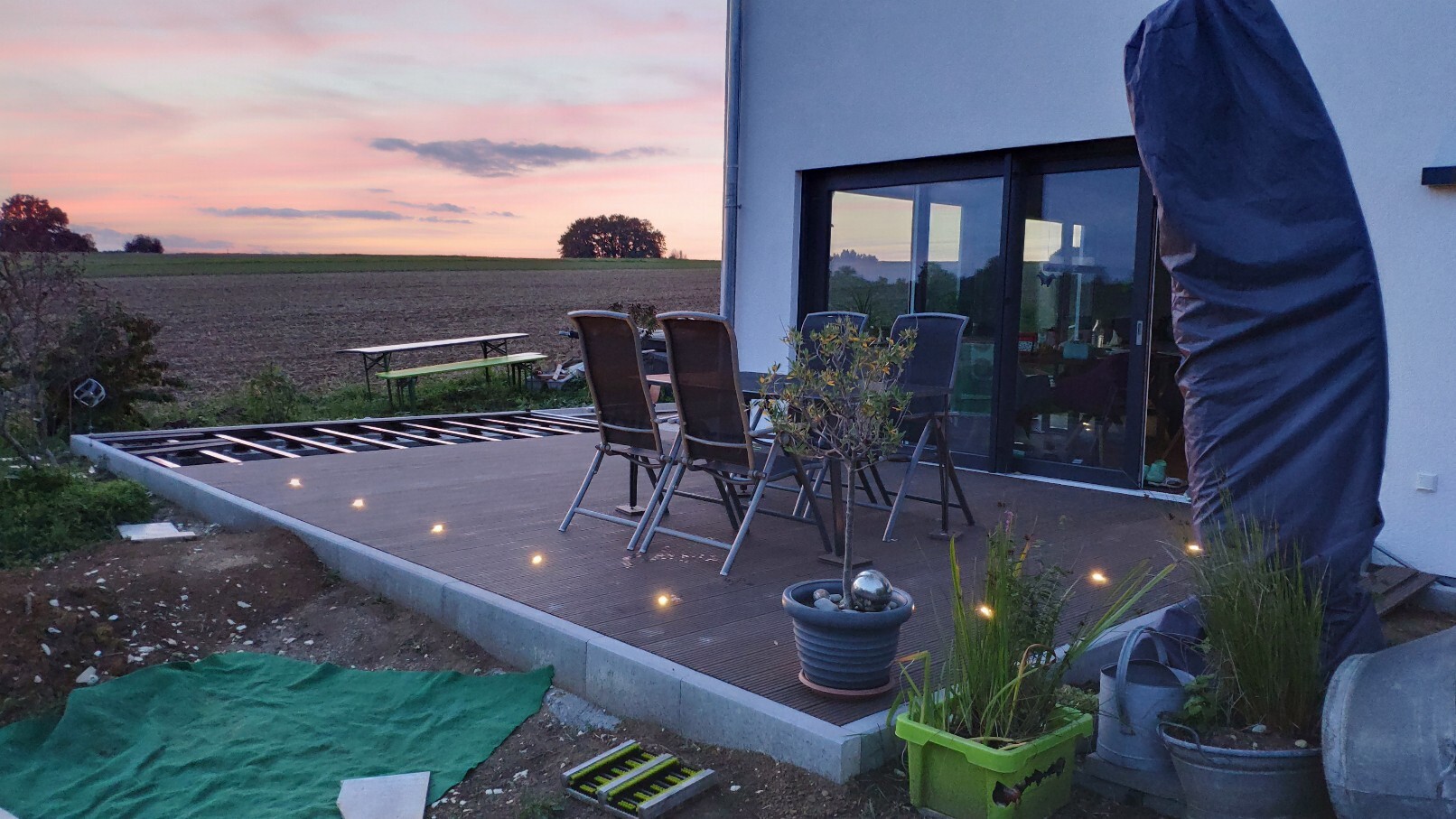 Terrace at the house with dining table and chairs, lighting, planters, sunset.