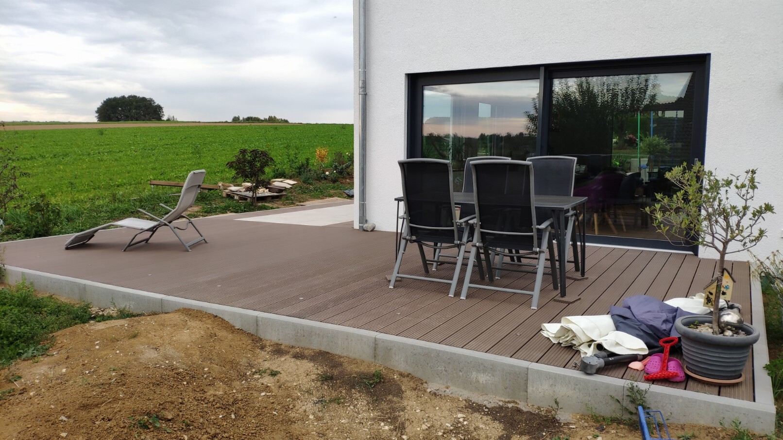 Modern wooden terrace with dining table and chairs in front of glass facade, view of fields.