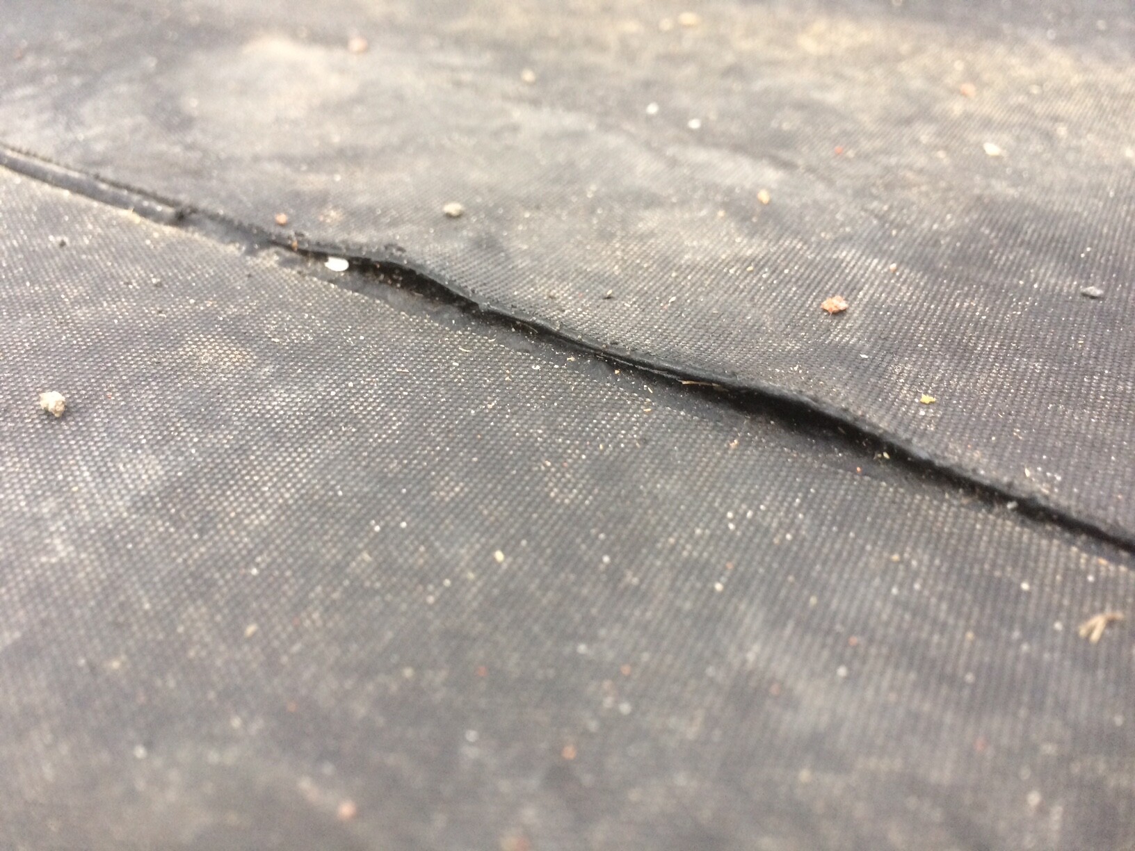 Close-up of a dark fabric with a torn seam and dust particles.