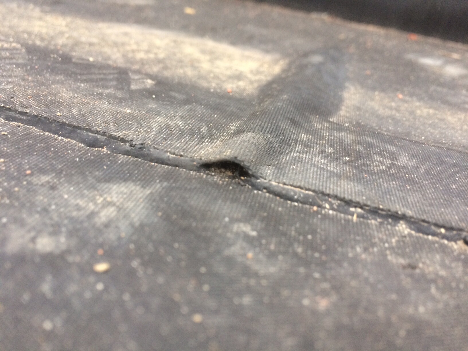 Close-up of a black membrane with a seam and a small hole; dusty.