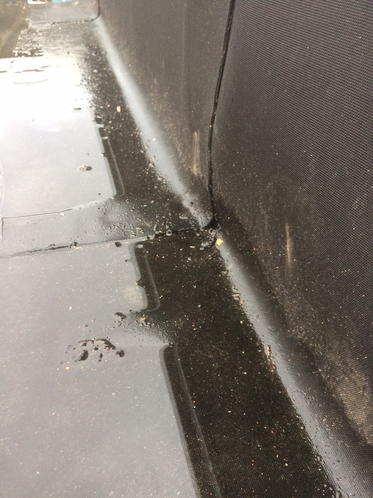 Close-up of a rain-wet roof edge with puddle of water between dark metal panels.