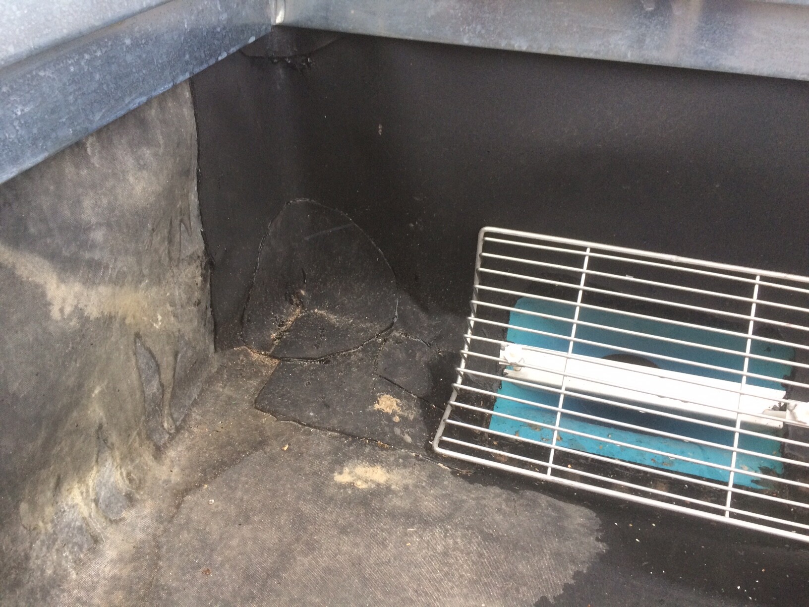 Dark interior of a grill with soot; a metal grill grate rests at an angle on a blue base.
