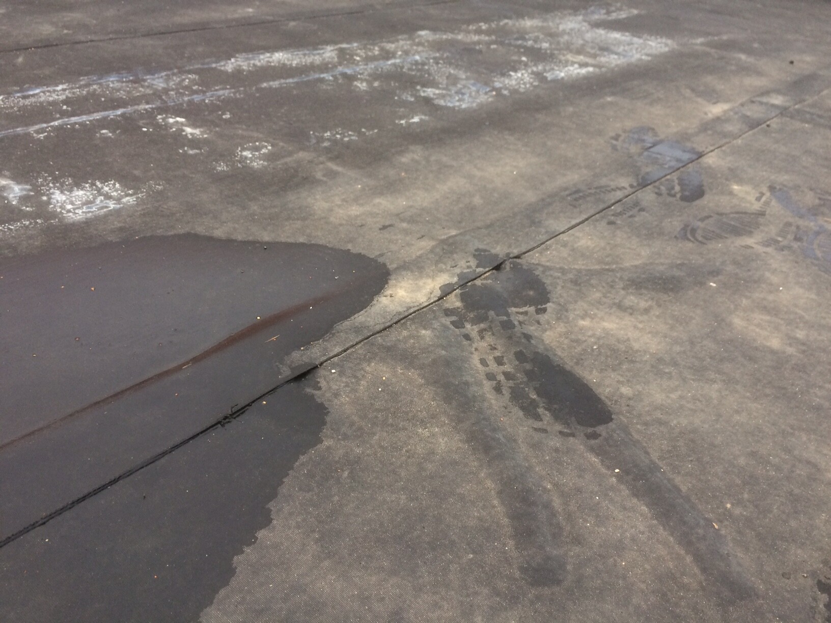 Wet asphalt surface with puddle on the left, dark stains and shoe prints on the right.