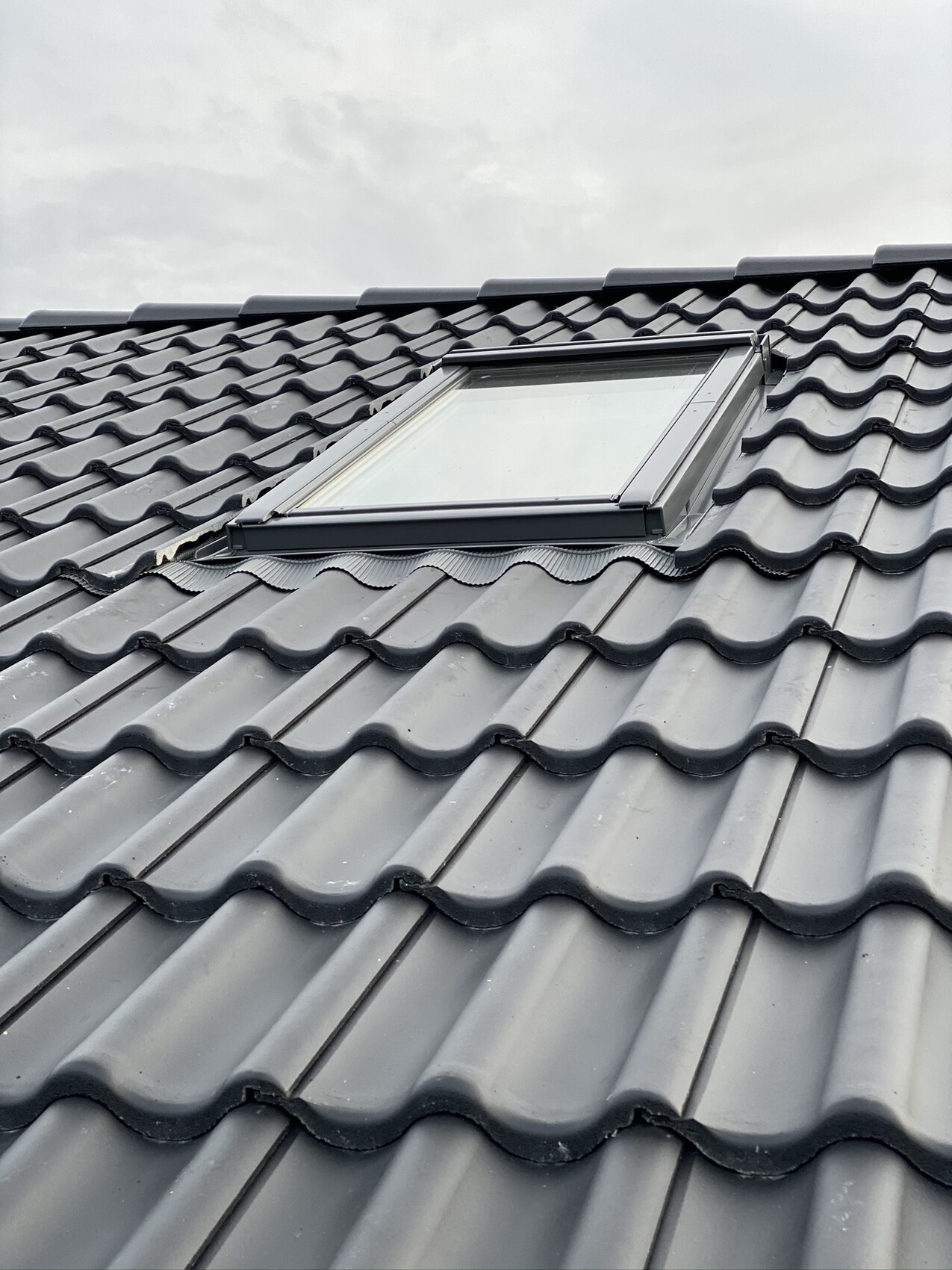 Roof with grey, wavy tiles and a large roof window on the slope.