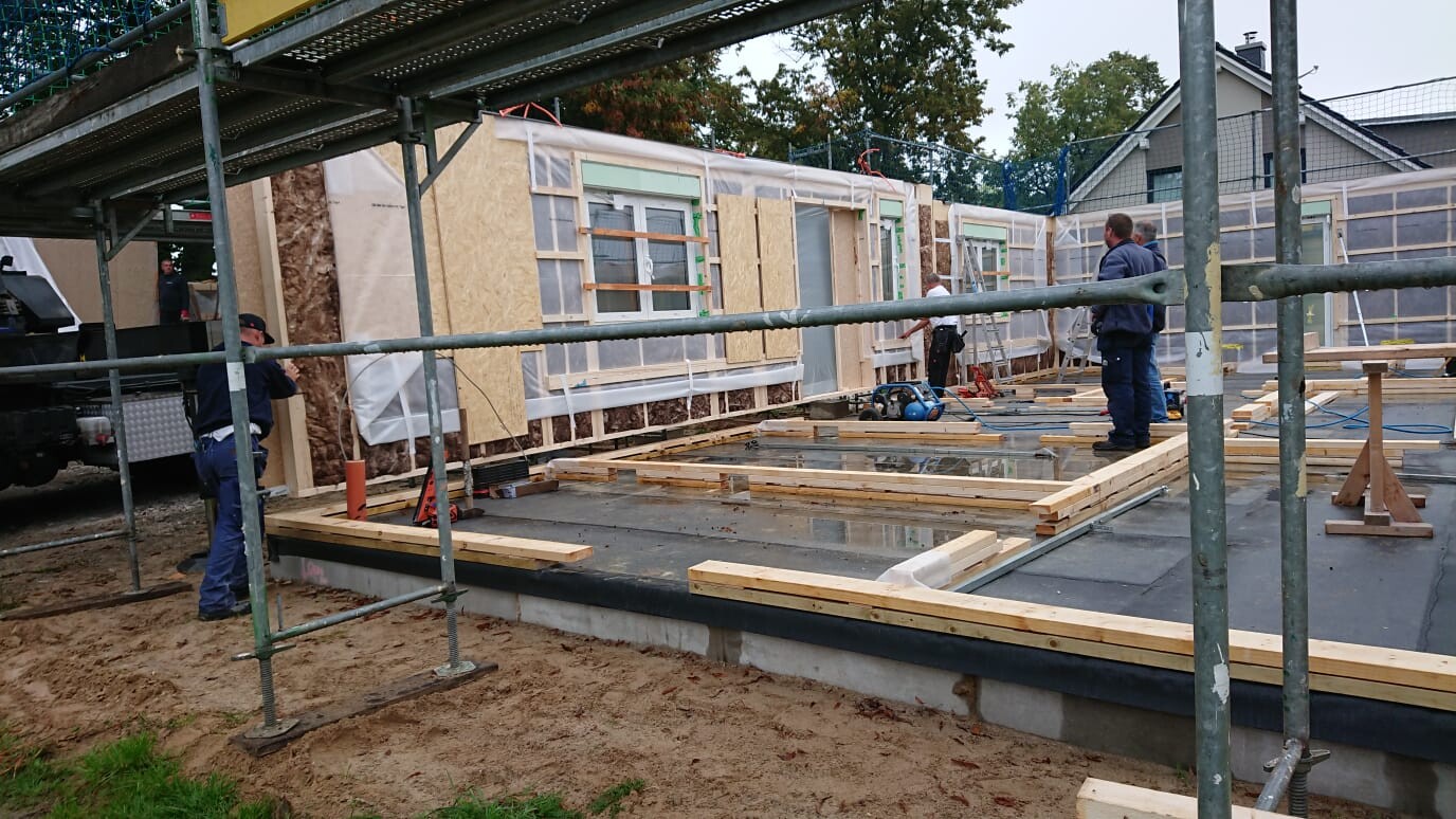 Construction site of a new house: wooden frame, scaffolding, construction workers on the foundation.