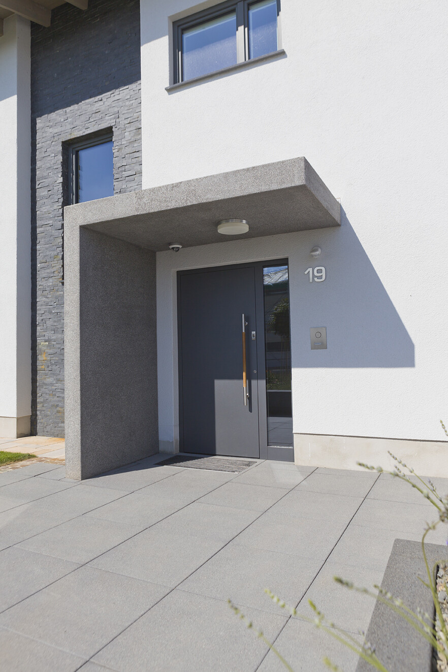 Moderne Hausfront mit dunkler Eingangstür, Überdachung und Hausnummer 19