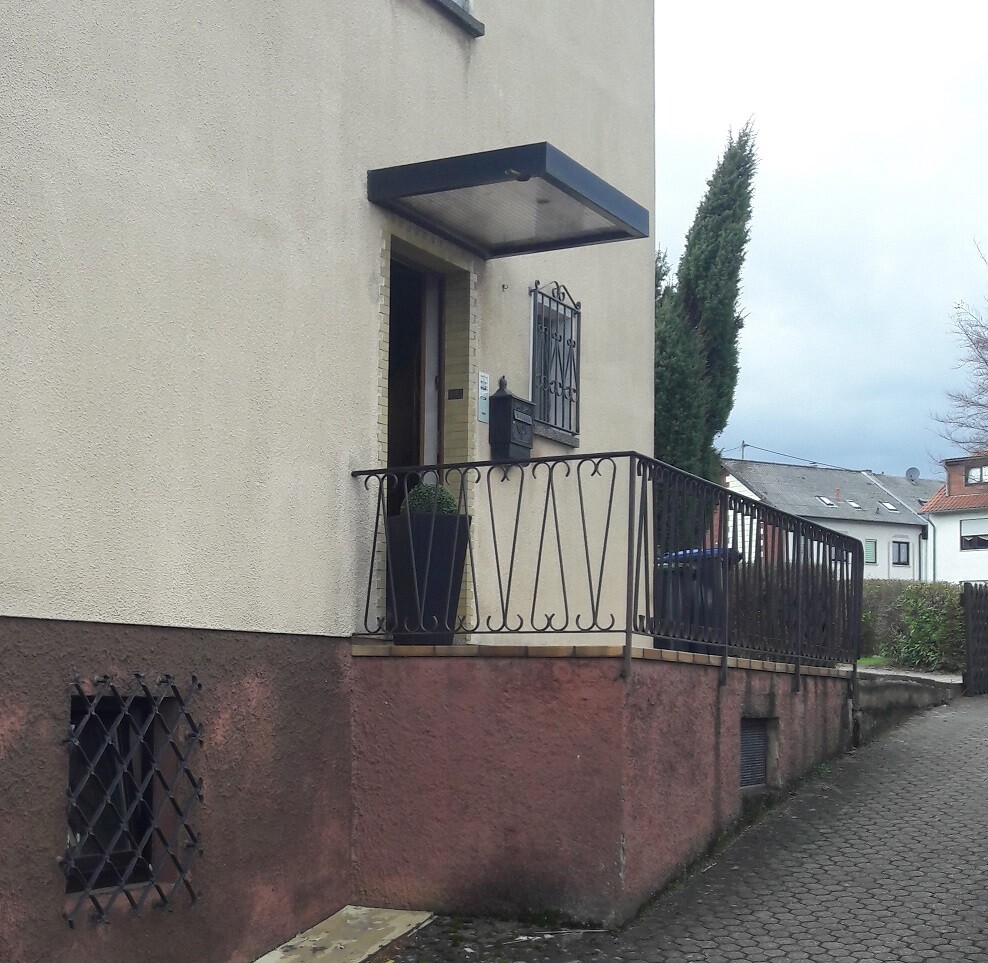 Entrance area of a residential building with a canopy, wrought iron railing, and planter.