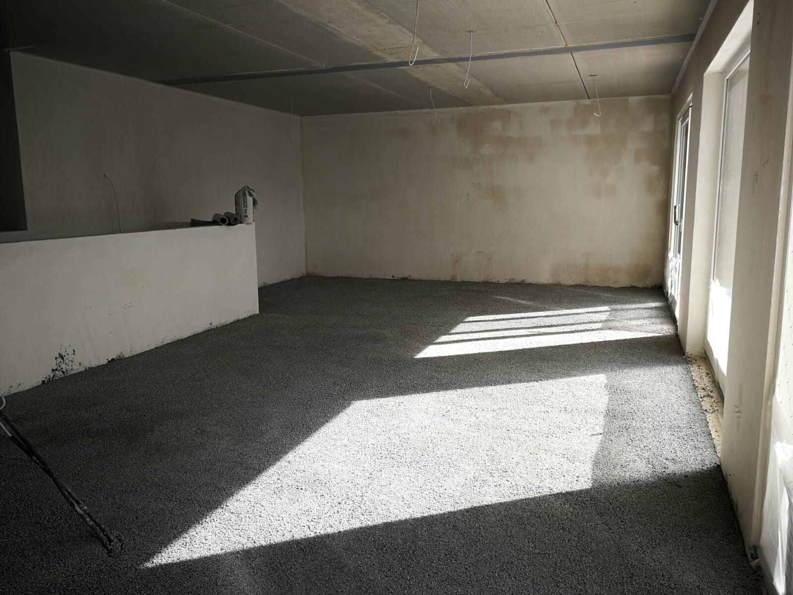 Empty construction room with white walls, gray floor, windows on the right and light-shadow.