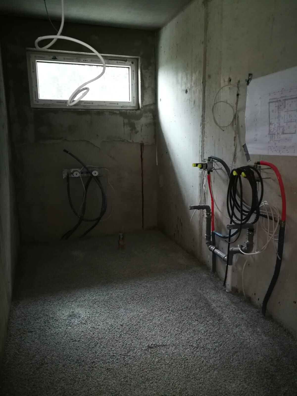 Small shell construction room with concrete walls, window top left, and various pipes and hoses.