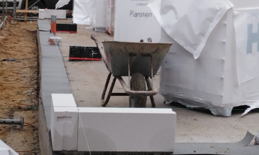 Construction site with wheelbarrow in front of foundation components and construction boards