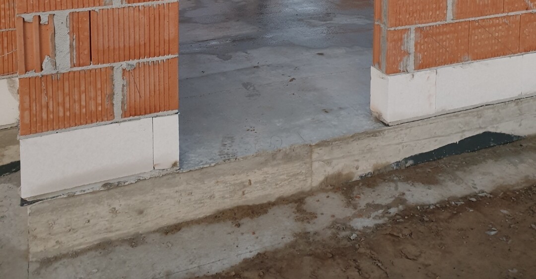 Unfinished building: two red brick columns with white base, door opening, concrete floor, soil in front.