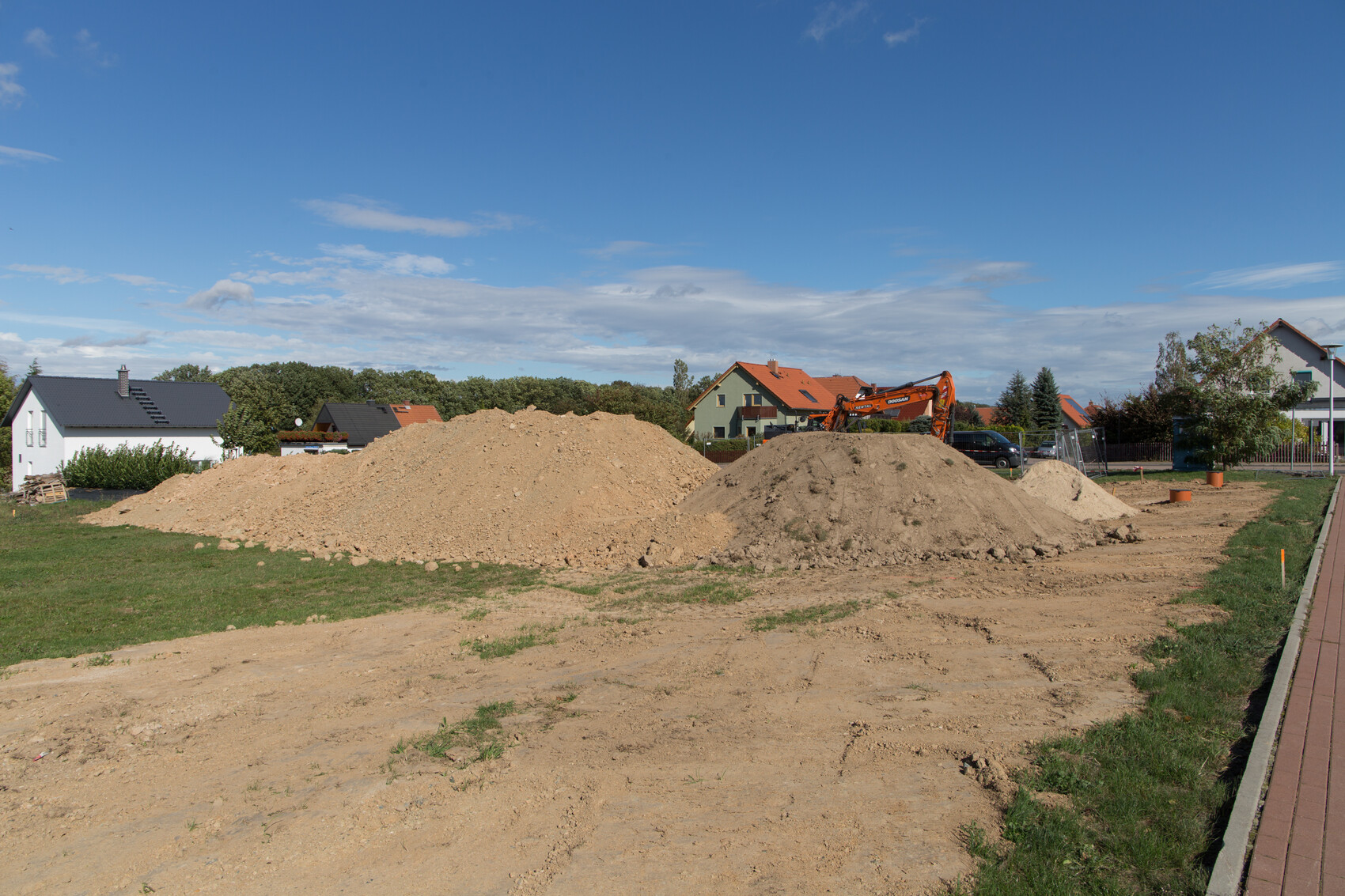 Baustelle mit Erdaushub, Bagger und Wohnhäusern unter blauem Himmel.