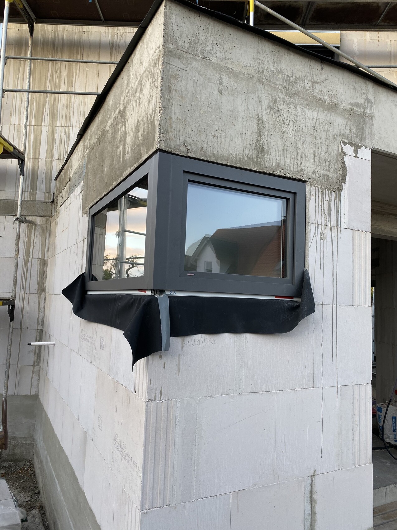 Exterior view of a new build: window with dark gray frame, below black protective covering.