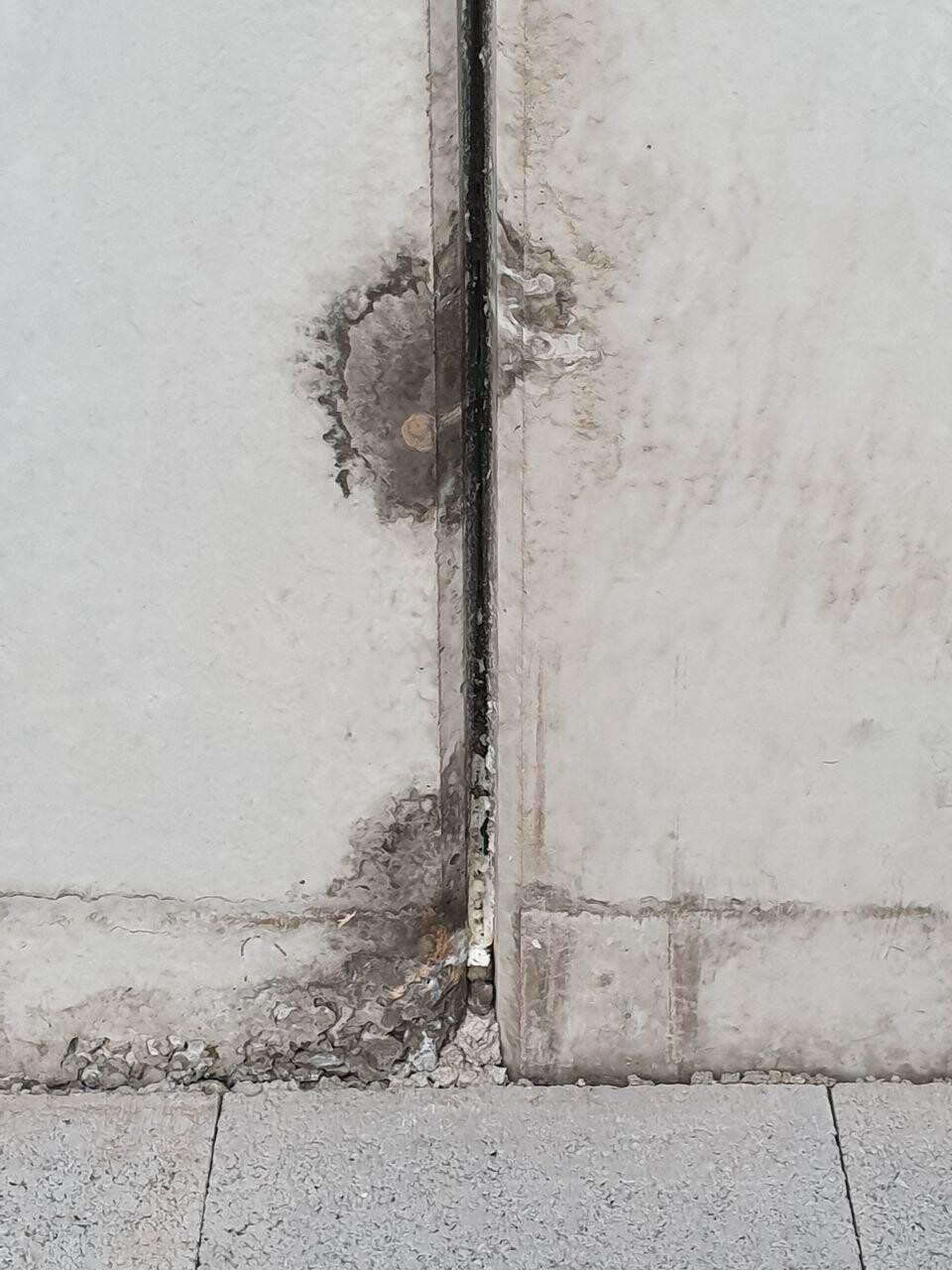 Close-up of a damaged concrete joint with cracks, spalling, and dust on the floor.
