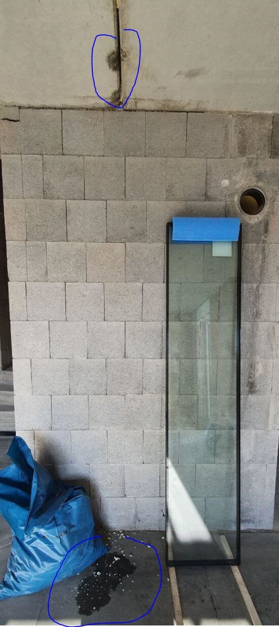 Glass pane leaning against concrete wall; blue bag on the floor; dark stain/liquid; hole in the wall.