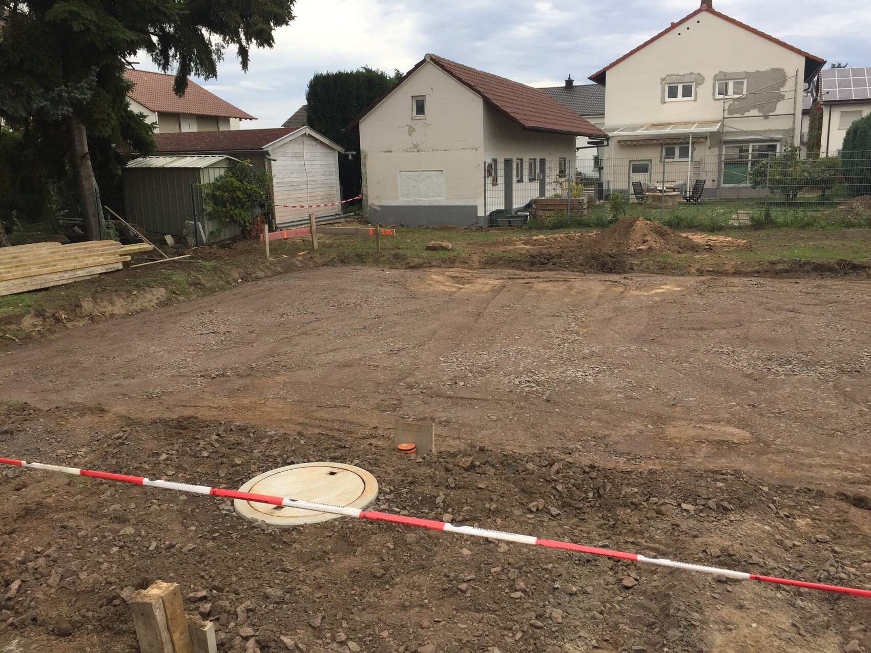 Construction site with earthworks, barrier tape, material stacks, and a round cover in the foreground