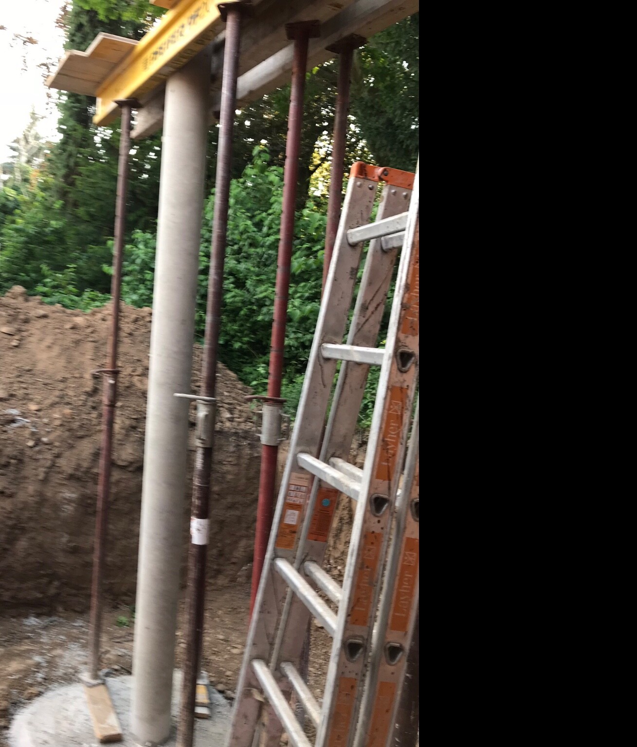 Construction site with support pipes, ladder and earth pit; wooden and metal structure