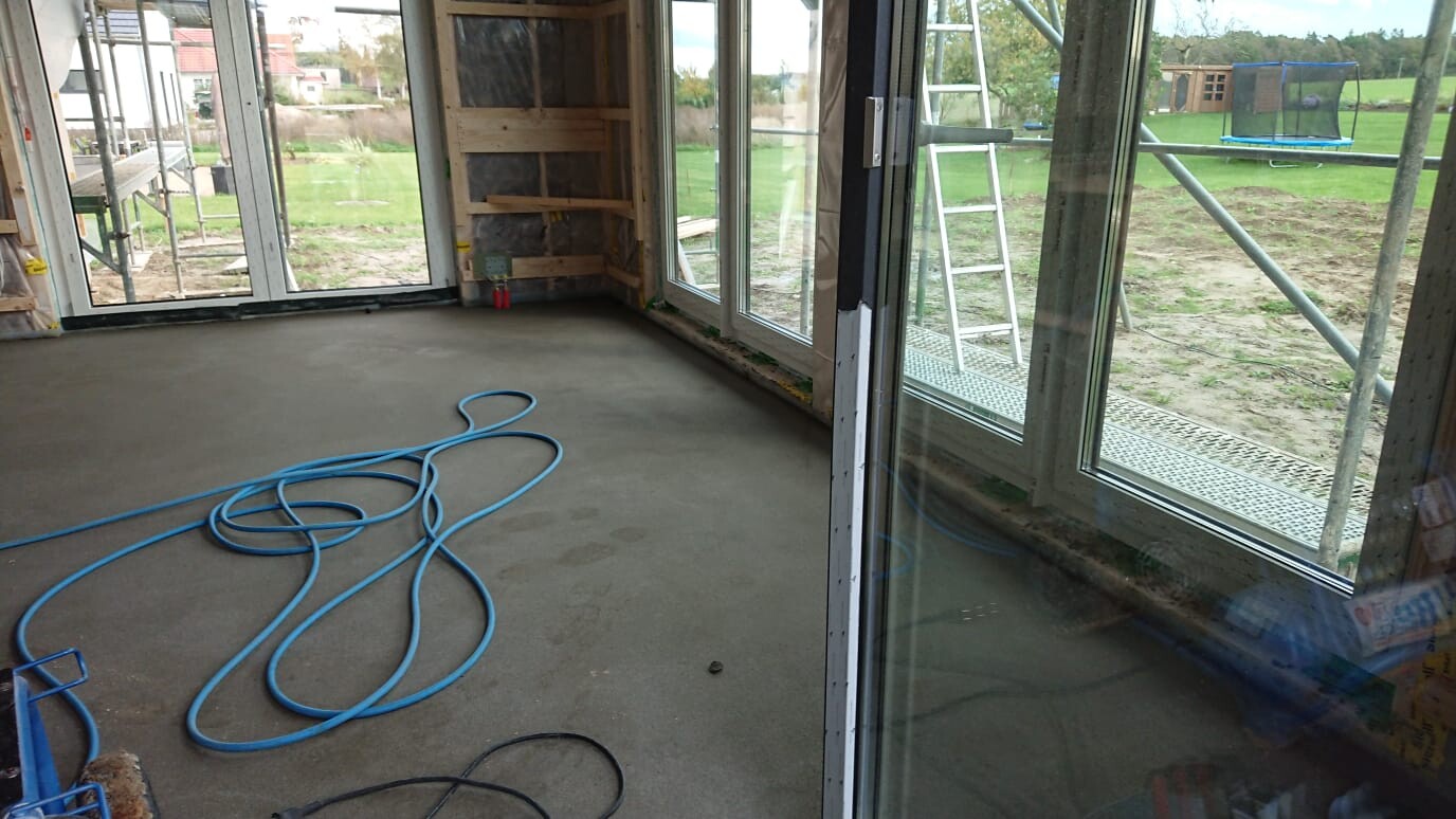 Unfinished interior of a construction site with blue hose on concrete floor, scaffolding outside.