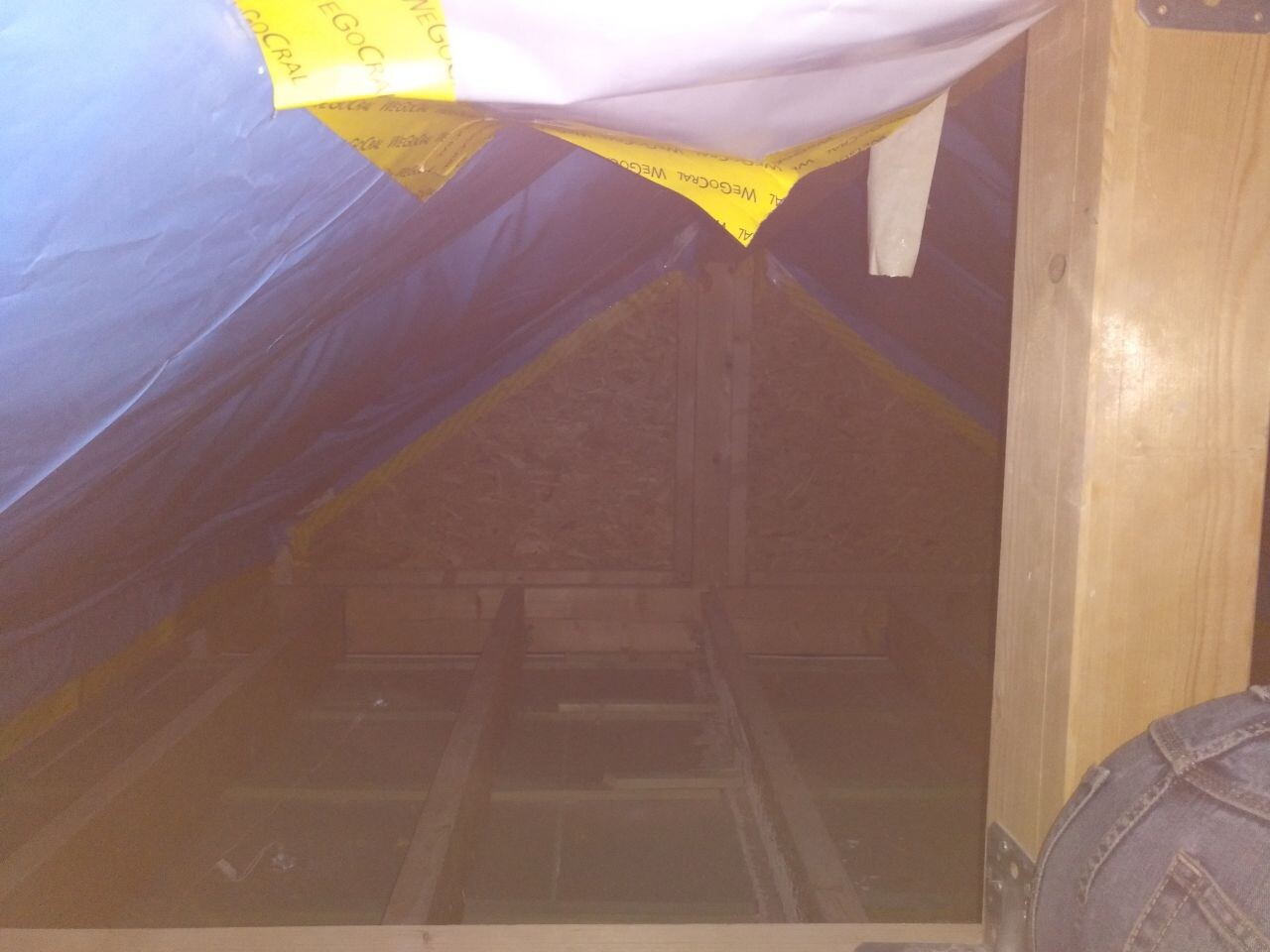 Dachboden mit Holzbalken, blauer Abdeckfolie und gelbem Isolierband; Blick auf Dachstuhl.