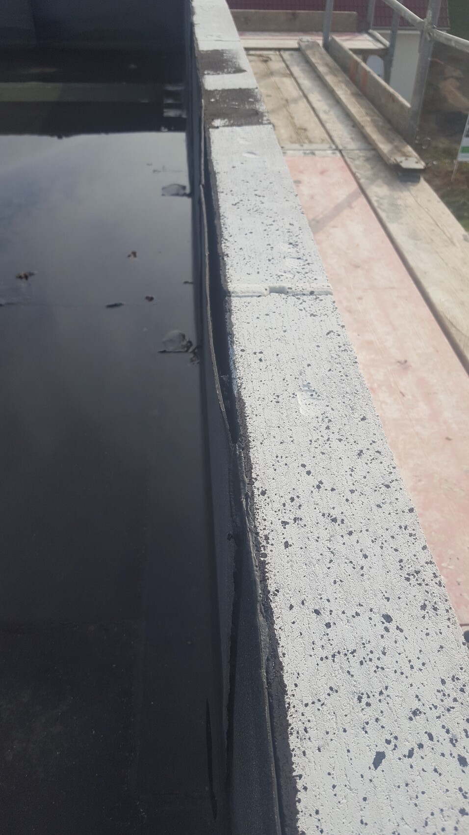 Baustelle am Dachrand mit Beton-Parapet, Holzbohlen und Gerüstarbeiten sichtbar