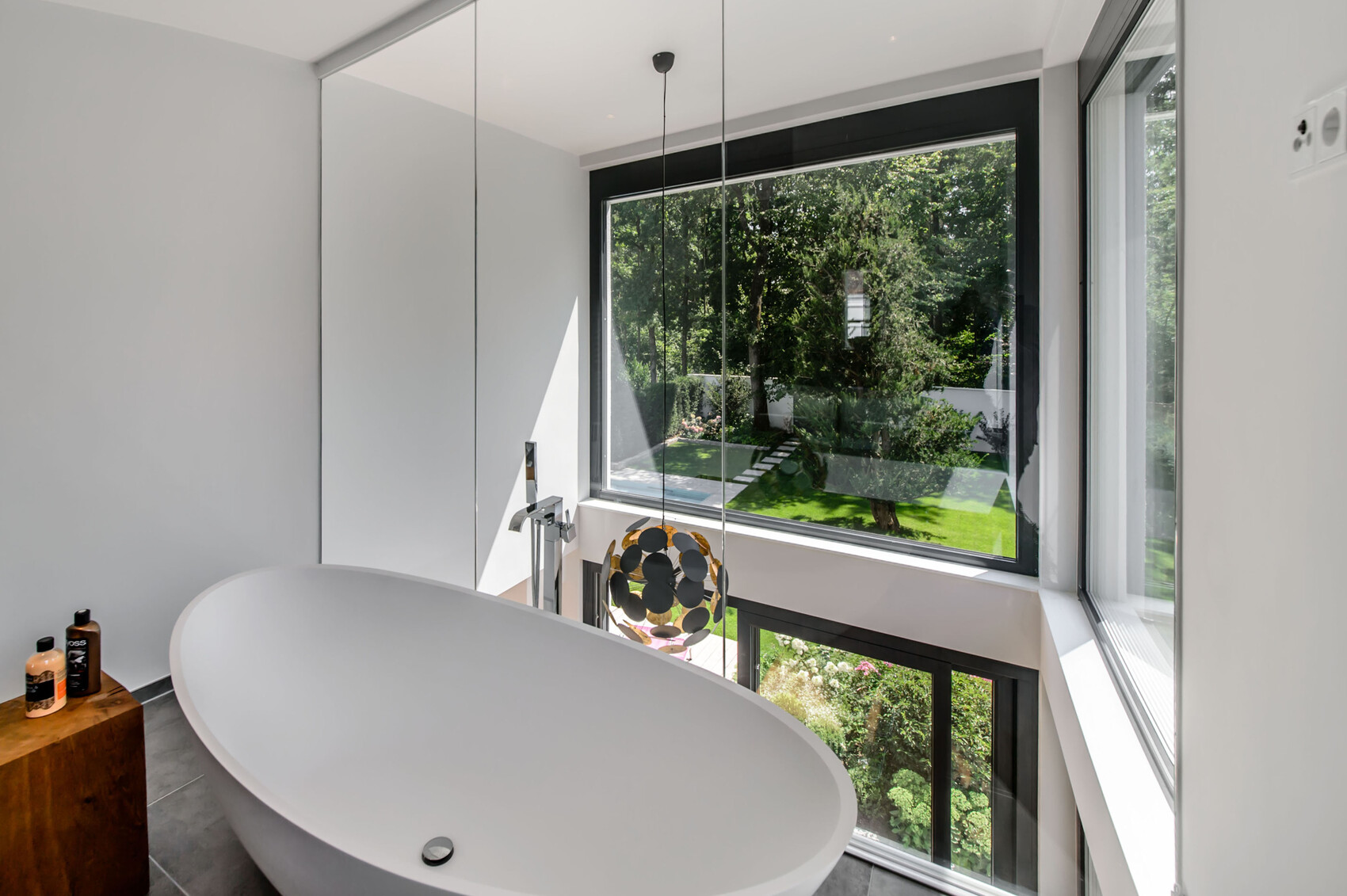 Modern bathroom scene with freestanding bathtub, large windows, and garden view.