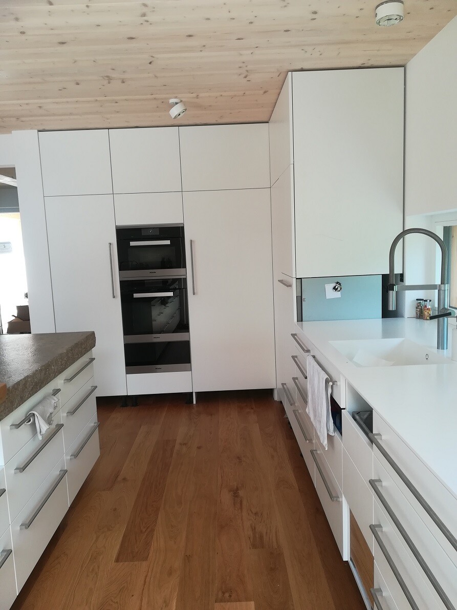 Moderne Weißküche mit Einbau-Backöfen, Spülbecken, Holzboden und Holzdecke.
