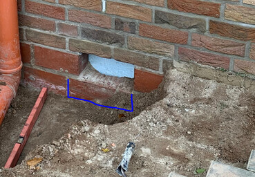 Outdoor construction site with brick wall, soil, foundation opening, blue marking
