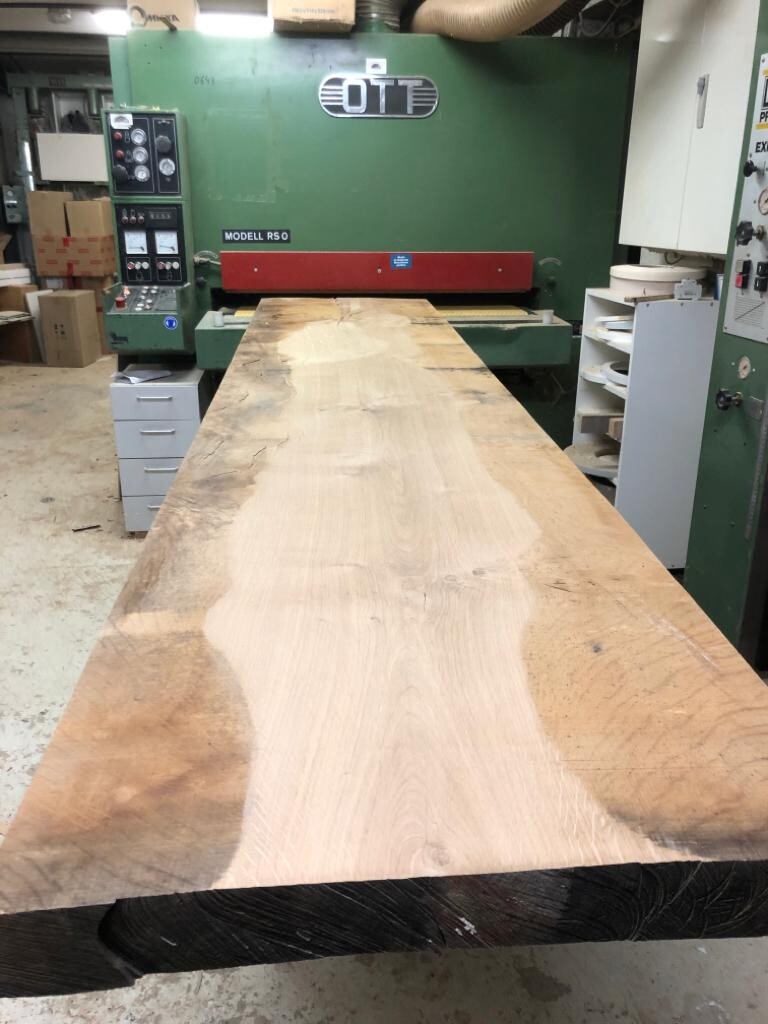 Long wooden plank lying on a large woodworking machine in a workshop.