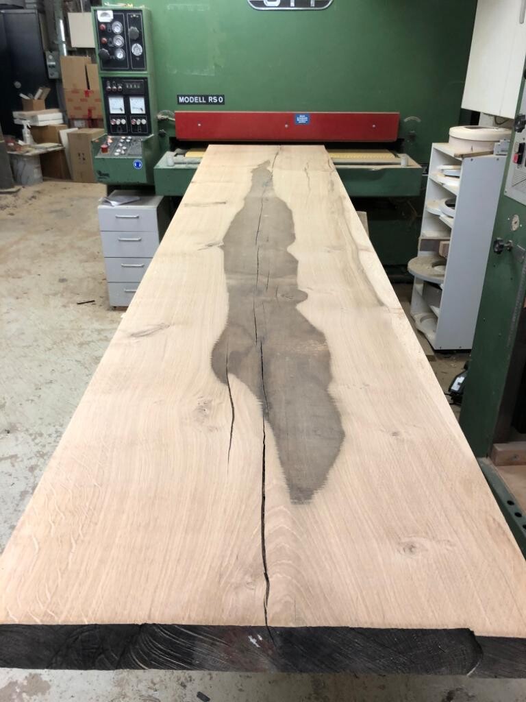 Large wooden board with a central crack and dark discoloration in a woodworking workshop.