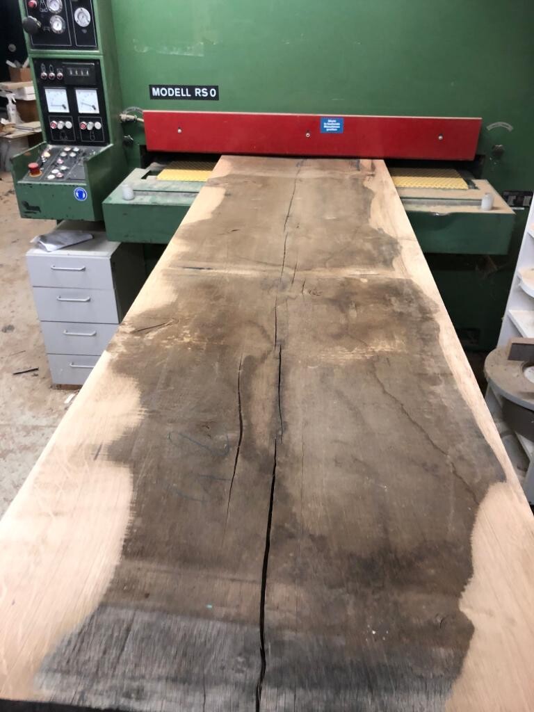 Long wooden board with a crack lying on a woodworking machine model RS0 in a workshop.