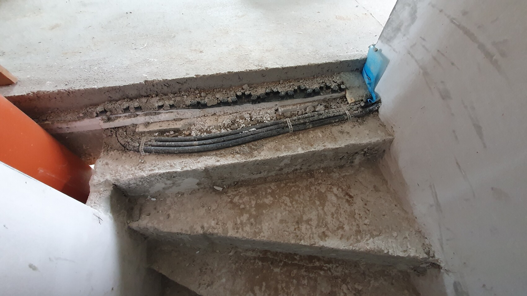 Baustelle: freiliegte Kabelrohre auf staubiger Treppe neben Betonrand.