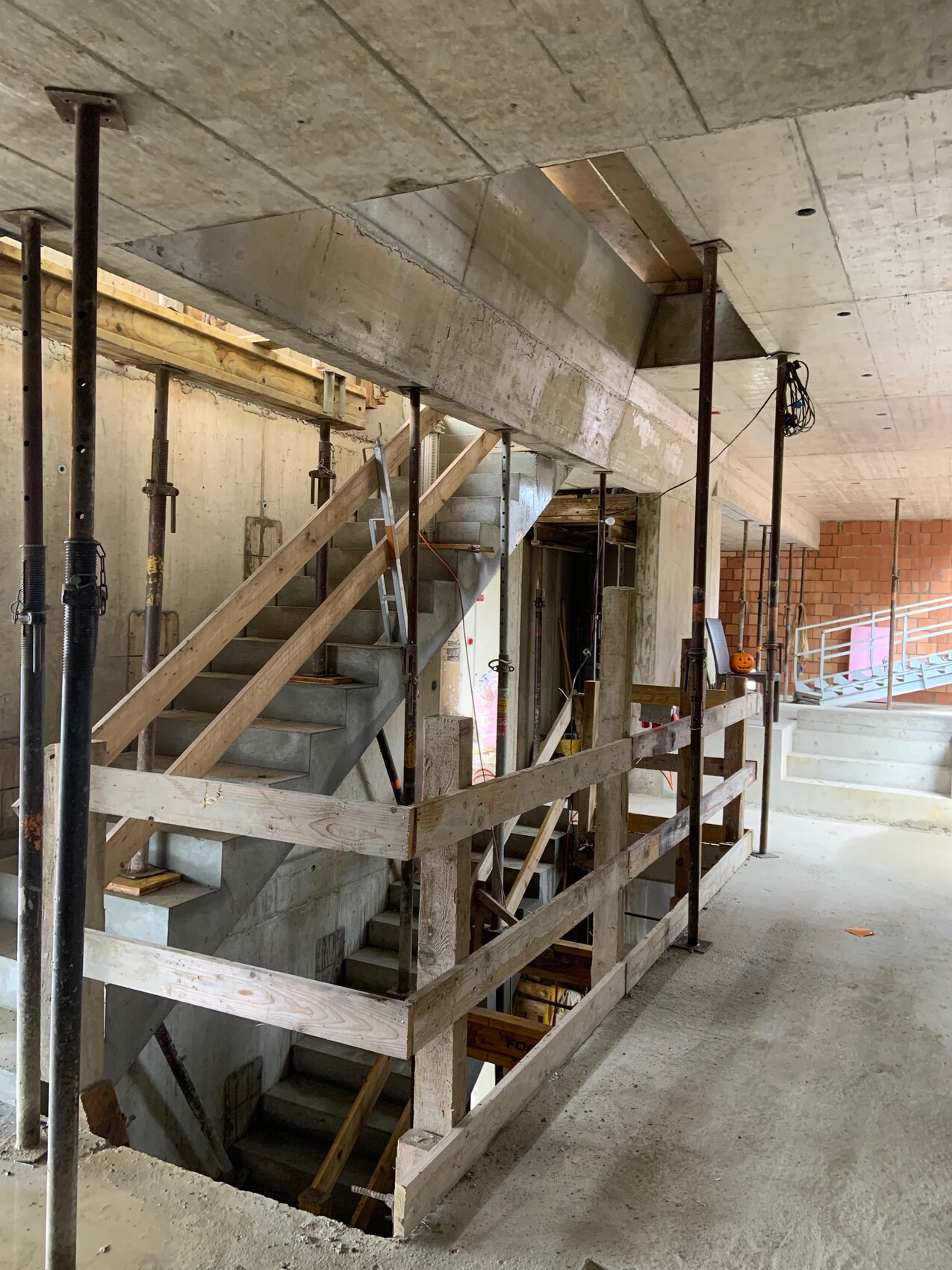 Interior photo of a construction site with temporary supports, wooden railings, and a concrete staircase.