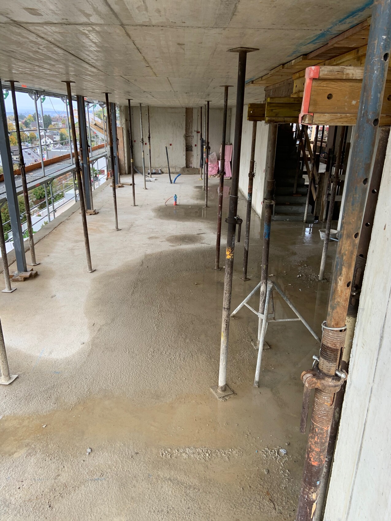 Interior of a construction site: supports, scaffolding, wet floor, wooden construction walls in the background.