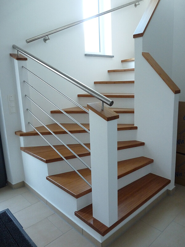 Modern interior staircase with wooden steps, stainless steel handrail, and white walls in the stairwell.