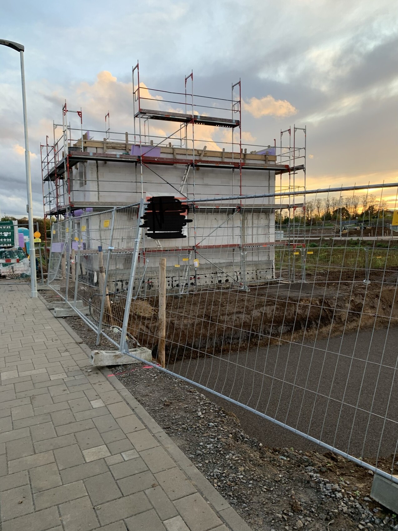 Baustelle mit Gerüst um einen Neubau; Bauzaun, Baugrube, Abendlicht